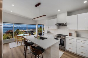 Una cocina moderna con una isla grande, muebles blancos, electrodomésticos de acero inoxidable y vista al mar.
