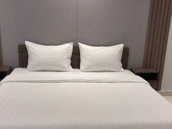 A bed with white bedding and two pillows, a wooden headboard, and a nightstand on each side.