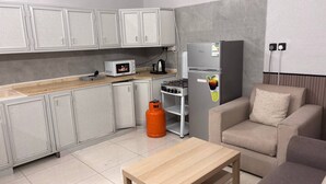 Een compacte keuken met een magnetron, gasfornuis en koelkast, een houten tafel en een bank.