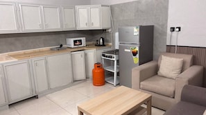 A compact kitchen with a microwave, gas stove, and refrigerator, a wooden table, and a sofa.