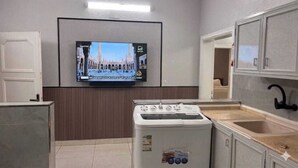 Een kleine keuken met een wasmachine, een spoelbak en een flatscreen televisie aan de muur.