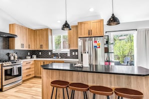 A modern kitchen with wooden cabinets, stainless steel appliances, and a central island with bar stools. - 4BR Mountain Retreat with Games, Large Deck &Views (Colorado Springs)