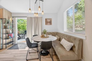 A modern living room with a round dining table, black chairs, a beige sofa, and a large window with blinds. - 4BR Mountain Retreat with Games, Large Deck &Views (Colorado Springs)