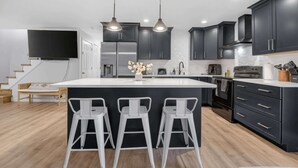 Una cocina moderna con armarios oscuros, una isla grande y tres taburetes de bar.