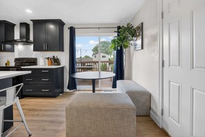A modern kitchen with dark cabinets, a round dining table, and a bench. - 4BR Spacious Home with Deck, BBQ,Fire Pit,Sleeps 8 (Arvada)