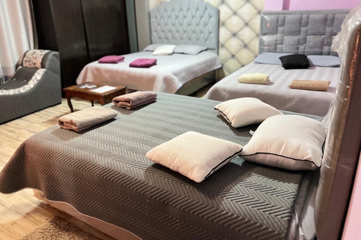 A hotel room with two beds, each with a different headboard design, and a seating area with a sofa and a chair.