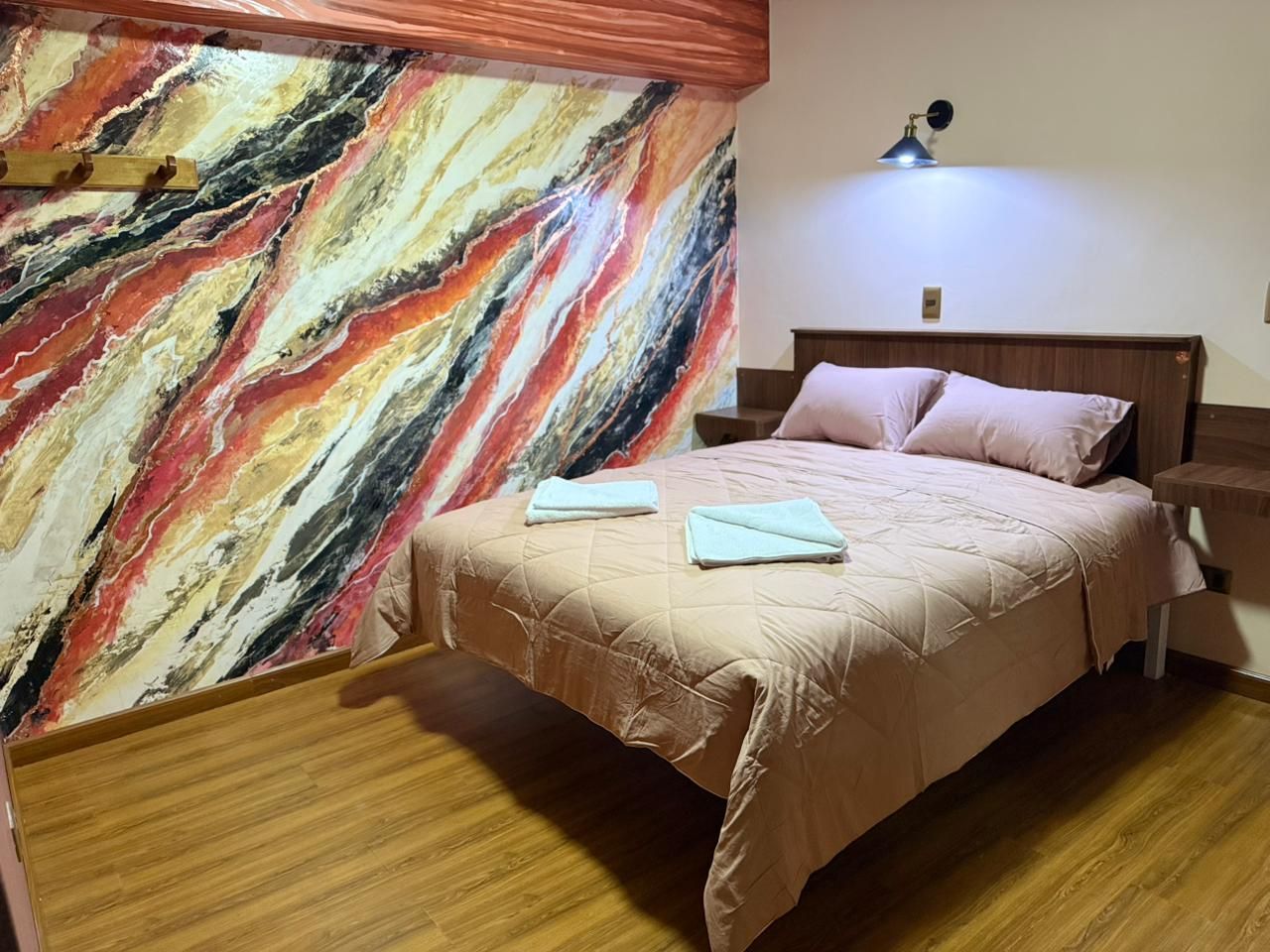 A bedroom with a bed, a nightstand, a lamp, and a marble wall.