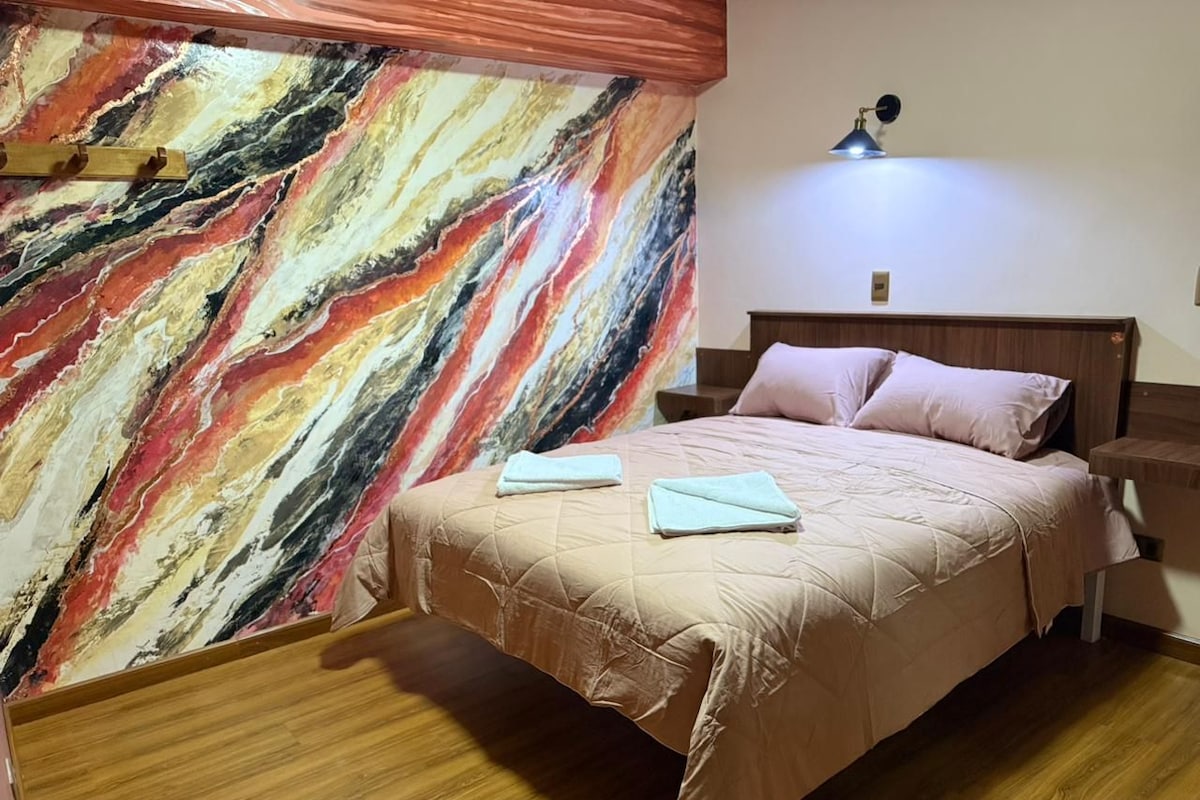 A bedroom with a bed, a nightstand, a lamp, and a marble wall.
