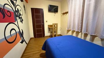 A room with a bed, a TV mounted on the wall, a wooden door, and a chair.