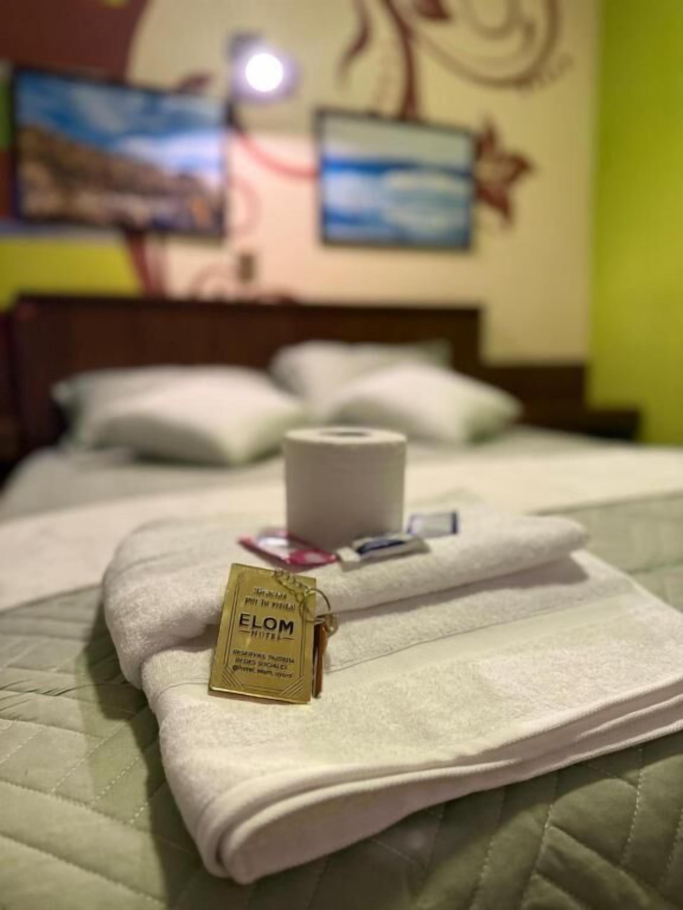 A neatly made bed with a folded towel and a keychain with the hotel name.