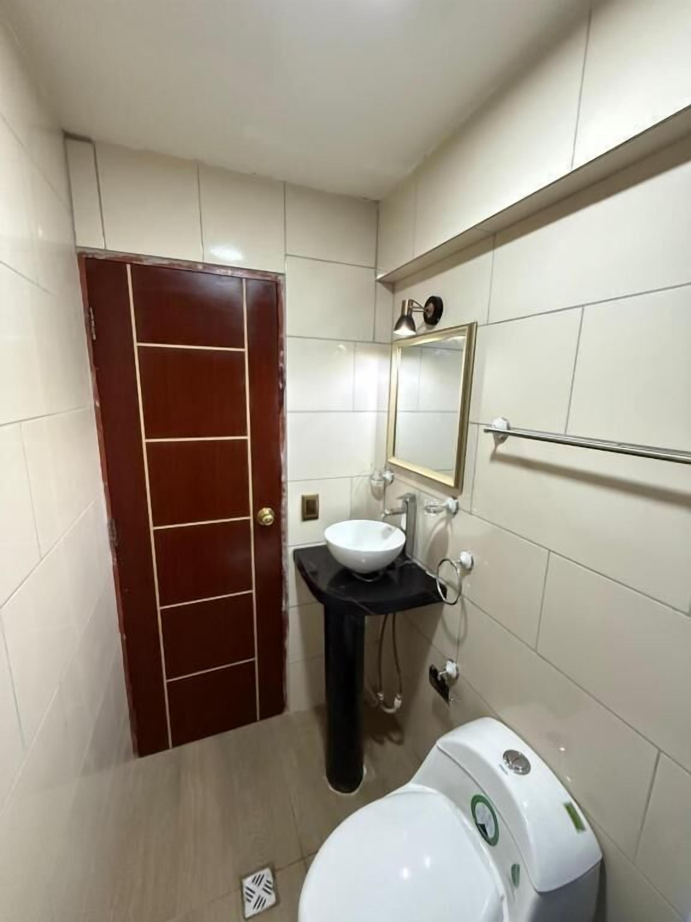 Un baño con inodoro blanco, lavamanos negro y un espejo sobre él.
