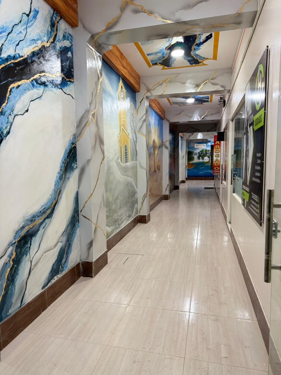 Corredor com detalhes nas paredes que imitam mármore, piso lustroso e teto com luminária.