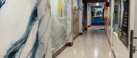 A hallway with marble-like wall designs, a polished floor, and a ceiling with a light fixture.