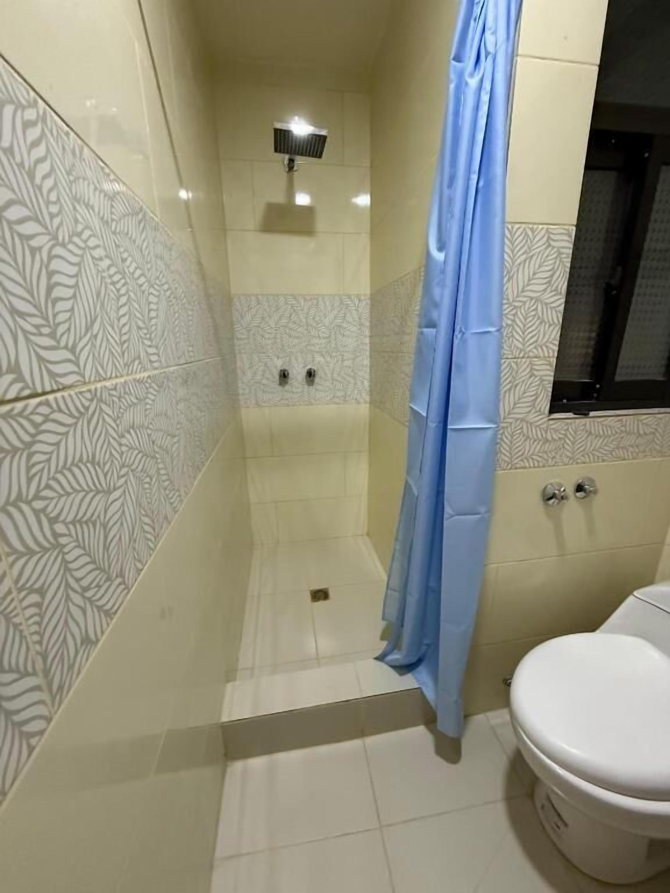 A bathroom with patterned tiles, a shower curtain, a toilet, and a wall-mounted light fixture.