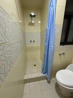 Un baño con baldosas estampadas, cortina de ducha, inodoro y aplique de pared.