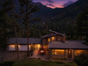 Ein zweistöckiges Haus mit Steinaußenwand, einer sichtbaren Garage und einer Terrasse mit Sitzgelegenheit.