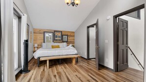 Une chambre à coucher avec un lit, un plancher en bois, un ventilateur sur pied et une porte.