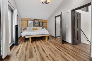 Ein Schlafzimmer mit einem Bett, Holzboden, einem Standventilator und einer Tür.