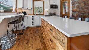 Une cuisine moderne avec des armoires blanches, un mur d’accent en pierre, un grand îlot central et une vue sur l’extérieur.