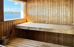 A wooden cabin with a bench by a window overlooking a lake.