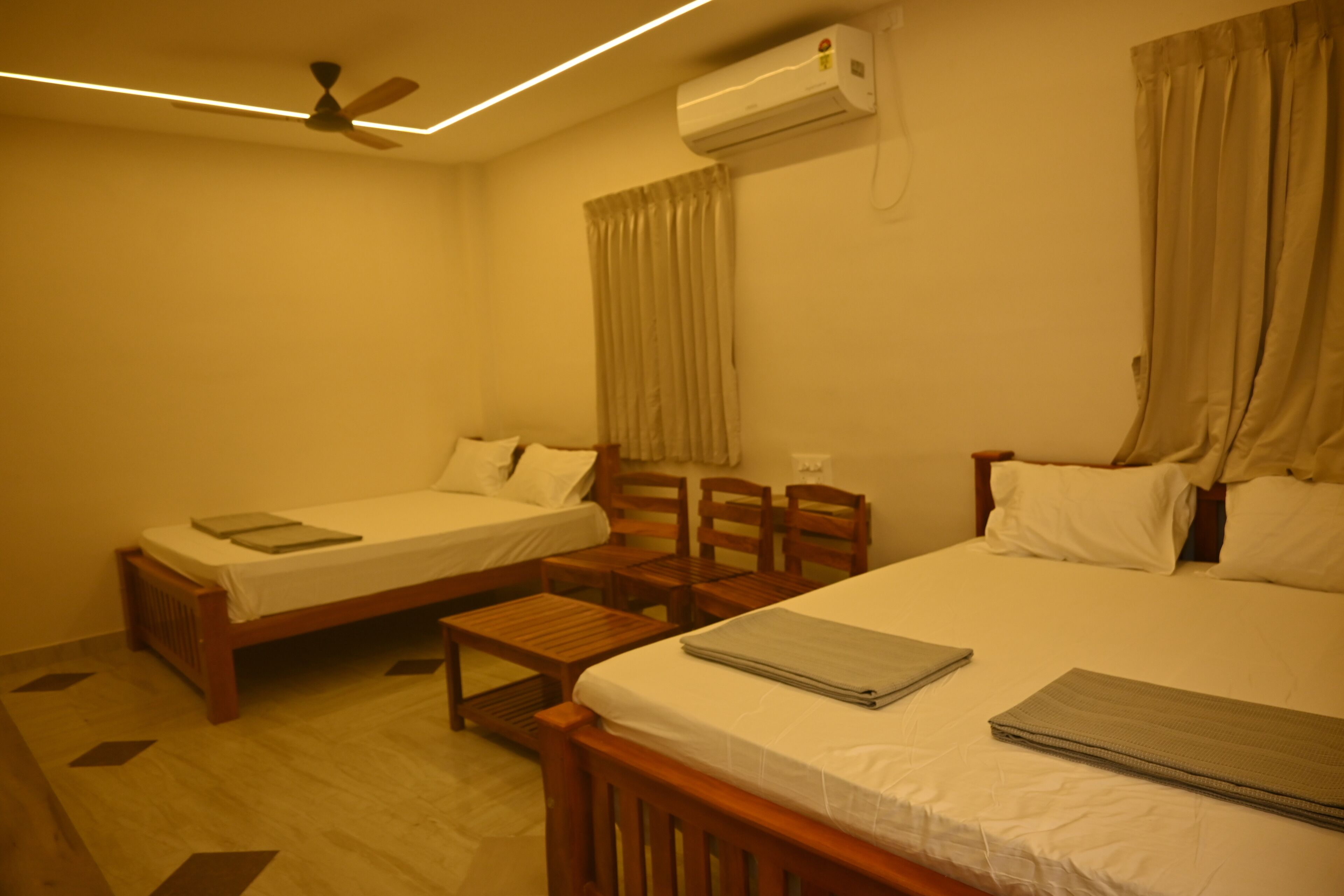 A hotel room with two beds, a ceiling fan, an air conditioner, and a wooden chair.