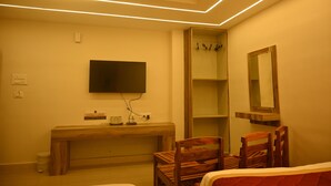 A bedroom with a bed, a wooden desk, a television, a mirror, and a shelf. - SANDALCITY HAVEN (Sathyamangalam)