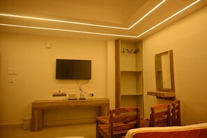 A bedroom with a bed, a wooden desk, a television, a mirror, and a shelf.