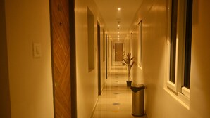 A hotel hallway with a wooden floor, a trash bin, and a potted plant. - SANDALCITY HAVEN (Sathyamangalam)