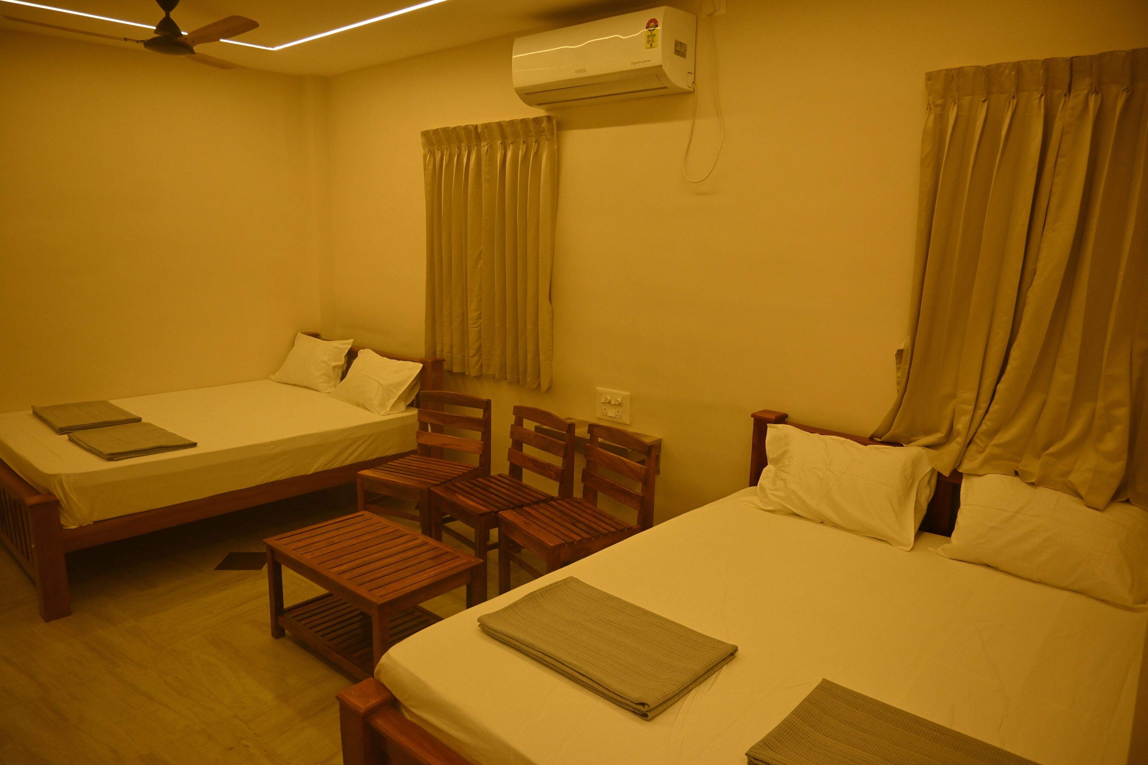 Una habitación de hotel con dos camas, una mesa de madera y un ventilador de techo.