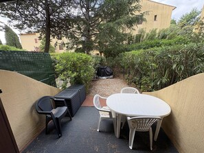 A patio with a table and chairs, a black outdoor sofa, and a black trash bin. - APPARTEMENT SAINT CLAIR (LE LAVANDOU)