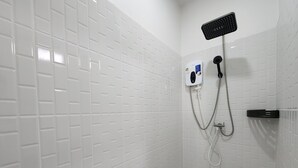 Un baño con paredes de azulejos blancos, una ducha con cabezal de mano y un panel de control.