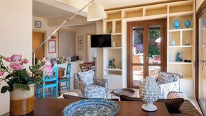 A living room with a wooden table, chairs, a television, and a bookshelf. - CORTE DELL'ULIVO| Sea View & Private Parking in Taormina Holiday Home (CAV) (Taormina)