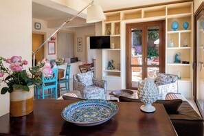 A living room with a wooden table, chairs, a television, and a bookshelf. - CORTE DELL'ULIVO| Sea View & Private Parking in Taormina Holiday Home (CAV) (Taormina)