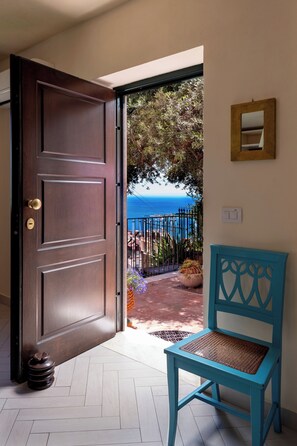 An open door leading to a balcony with a view of the sea, a blue chair, and a potted plant. - CORTE DELL'ULIVO| Sea View & Private Parking in Taormina Holiday Home (CAV) (Taormina)