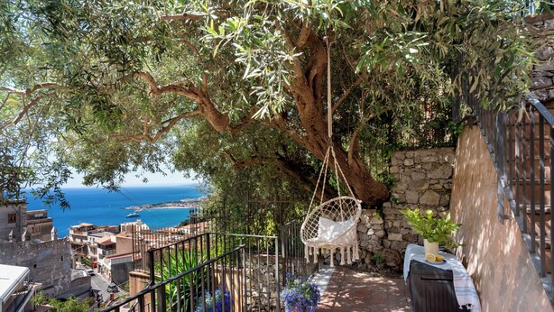 A stone wall, a hanging chair, a table with a plant, and a view of the sea. - CORTE DELL'ULIVO| Sea View & Private Parking in Taormina Holiday Home (CAV) (Taormina)