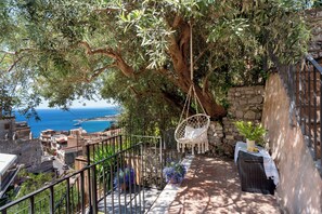 A stone wall, a hanging chair, a table with a plant, and a view of the sea. - CORTE DELL'ULIVO | Ocean View & Private Parking in Taormina Vacation Home (CAV) (Taormina)