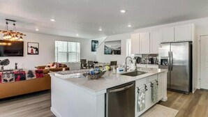 A modern kitchen with a central island, stainless steel appliances, and a dining area with a sofa. - Spacious 4BR Home Near Denver & DIA (Thornton)