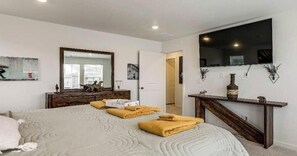 Une chambre à coucher avec un grand lit, une commode en bois, un miroir et un téléviseur fixé au mur.