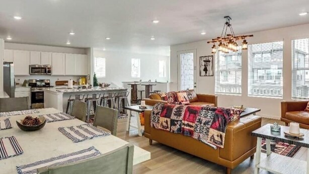 A spacious living area with a sofa, coffee table, and dining table set with placemats. - Spacious 4BR Home Near Denver & DIA (Thornton)
