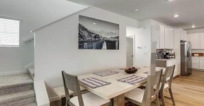 Une cuisine moderne avec des meubles blancs, un réfrigérateur en acier inoxydable et un coin repas avec une table dressée pour quatre personnes.