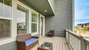 A balcony with a wicker sofa, a glass table, and a view of a parking lot. - Spacious 4BR Home Near Denver & DIA (Thornton)