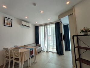 A modern living room with a sofa, dining table, chairs, and a TV. - 芭堤雅市中心 奥林巴斯城市花园 近步行街和海滩的水系公寓 泳池景观 可带榴莲和山竹 阳台可吸烟 (Muang Pattaya)