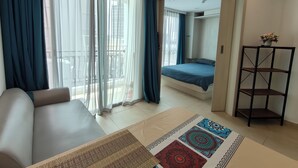 Ein modernes Hotelzimmer mit einem großen Bett, einer Sitzecke, einem kleinen Schreibtisch und Blick durch ein großes Fenster.