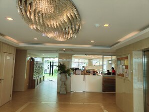 A hotel lobby with a large chandelier, a reception desk, and a view of the garden outside. - 芭堤雅市中心 奥林巴斯城市花园 近步行街和海滩的水系公寓 泳池景观 可带榴莲和山竹 阳台可吸烟 (Muang Pattaya)