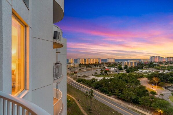 A high-rise building with balconies, a cityscape with illuminated buildings, and a sunset sky. - Summer Ending 15% off – Gulf Views, Pool, Hot tub, Tennis, Pickle Ball ++ (Destin)