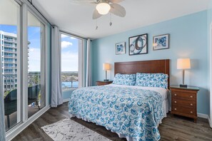 A bedroom with a large window, a bed with patterned bedding, two bedside lamps, and artwork on the wall. - Gulf views ~ Updated unit ~ Beach access ~ Pool, Hot tub, Tennis, Pickle Ball ++ (Destin)