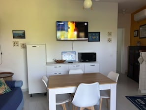 Eine moderne Küche mit einem Holzespeisetisch, weißen Stühlen, einer Mikrowelle und einem Fernseher, der über der Arbeitsfläche angebracht ist.