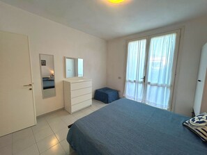 Ein Schlafzimmer mit Bett, Schminktisch, Spiegel, Fenster mit Vorhängen und einer Tür.