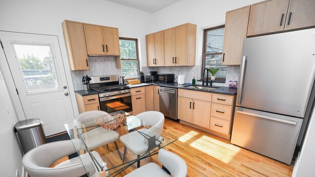 Eine moderne Küche mit Holzschränken, Edelstahlgeräten, einem Glastisch und Blick ins Freie.