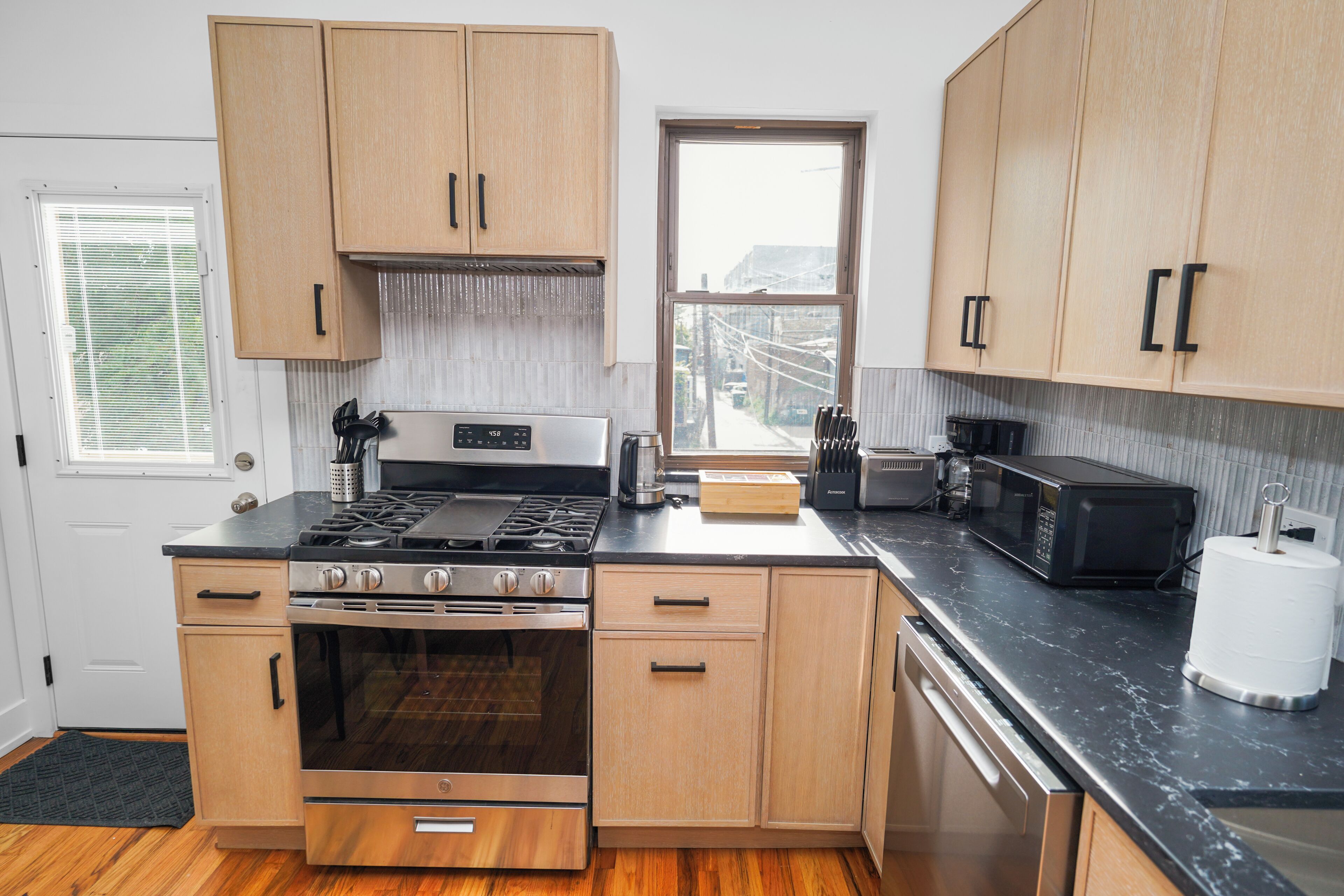 A kitchen with wooden cabinets, a stove, oven, microwave, and a window.